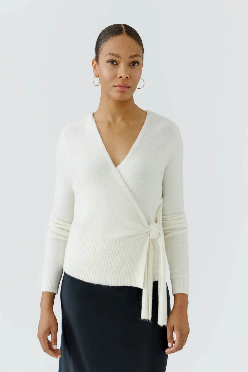 Woman in white wrap cardigan, paired with a black skirt, standing confidently.