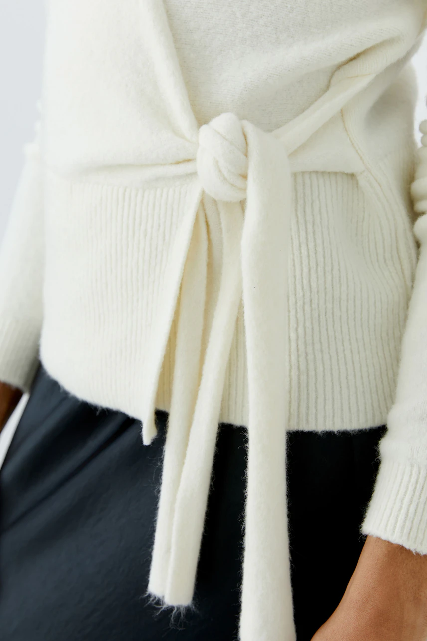 Woman in a white cardigan with a tie-front detail, paired with a dark skirt. Casual and stylish look.