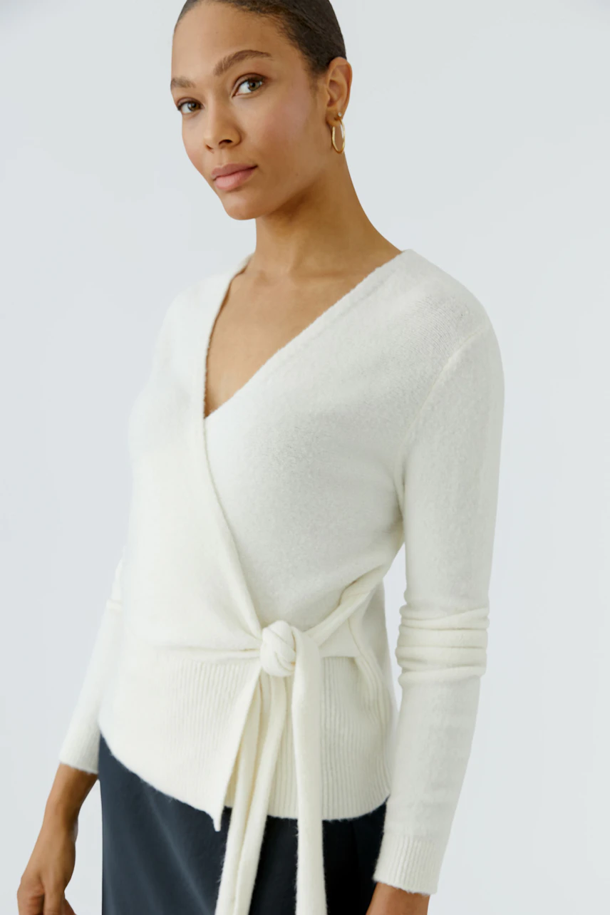 Woman in white cardigan: A wrap-style knit cardigan with a tie detail, paired with a black skirt.