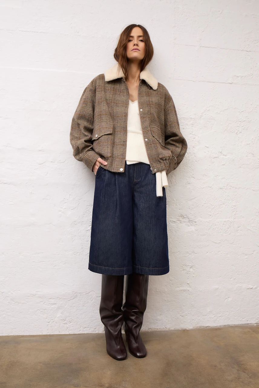 Woman in cozy cardigan, paired with a plaid jacket, denim skirt, and knee-high boots, exuding casual style.