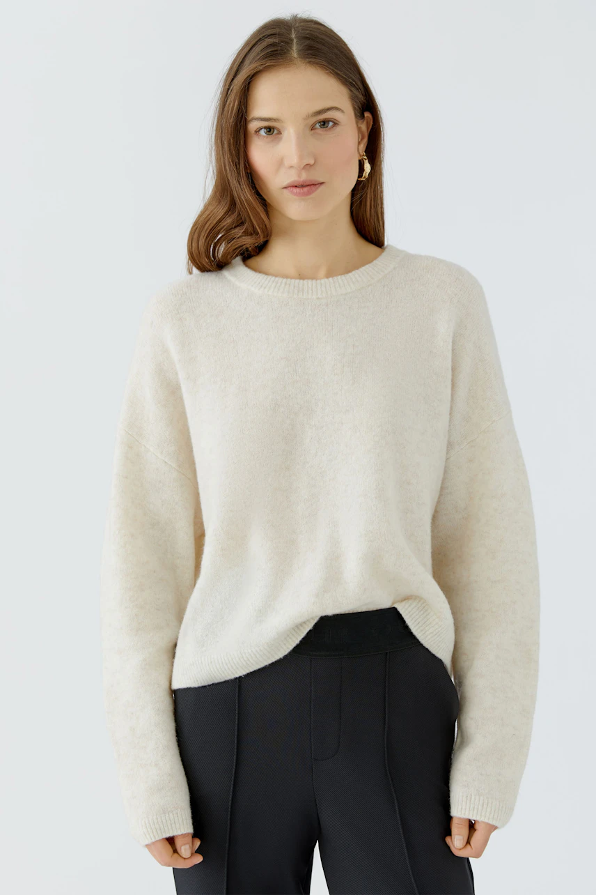Casual women's pullover: Woman in a soft beige pullover paired with black pants, exuding relaxed style.
