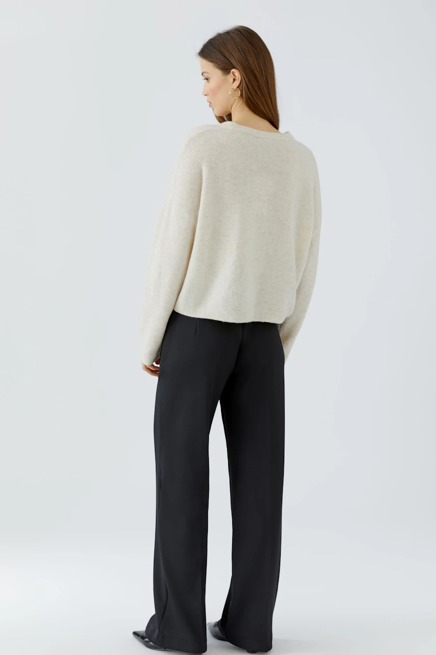 Casual women's pullover: Woman in a cream pullover and black pants, viewed from the back.