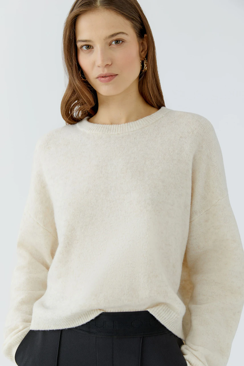 Casual women's pullover: Woman in a cream pullover with relaxed fit, paired with dark trousers.