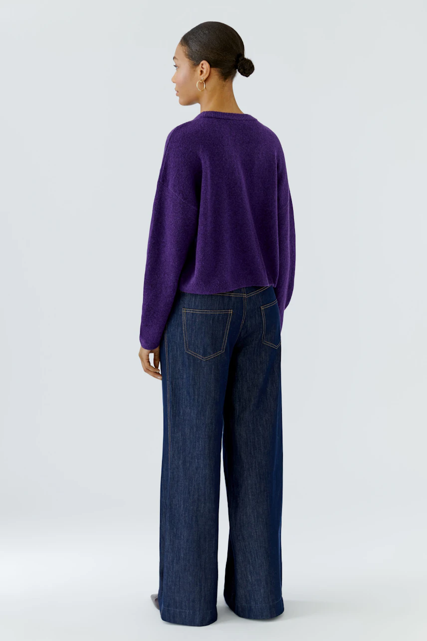 Casual women's pullover: Woman in a purple pullover and wide-leg jeans, viewed from the back.