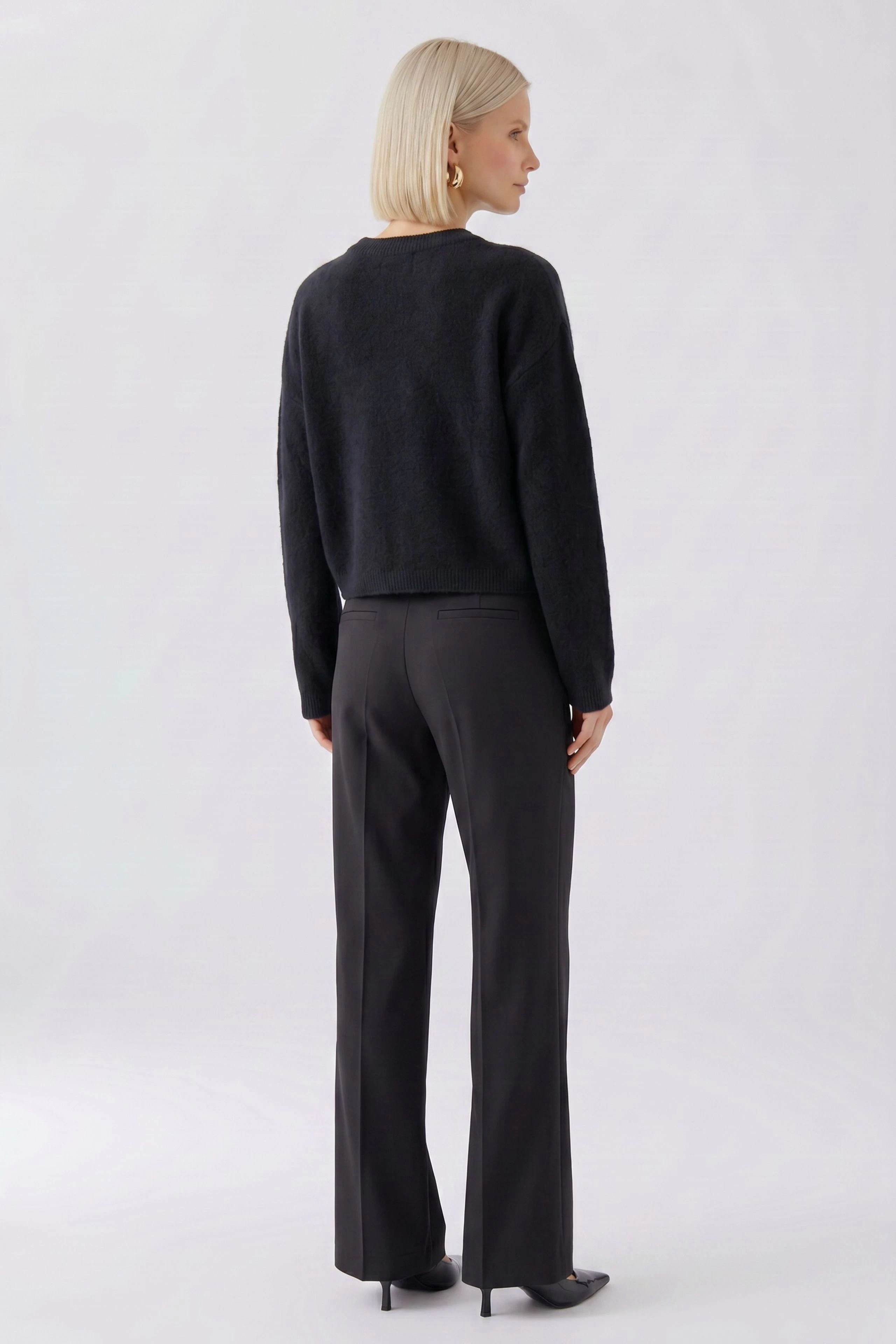 Frau im schwarzen Pullover, Rückansicht. Schlichtes Design, kombiniert mit dunkler Hose.