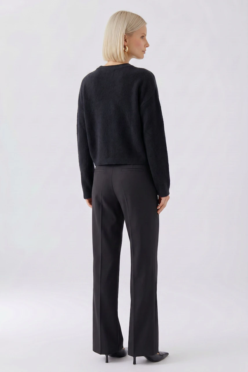 Frau im schwarzen Pullover, Rückansicht. Schlichtes Design, kombiniert mit dunkler Hose.