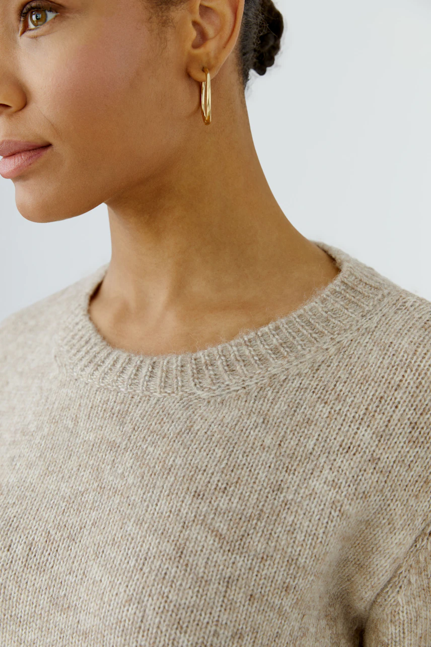 Casual pullover: Woman in a beige knit pullover with hoop earrings, showcasing a relaxed style.