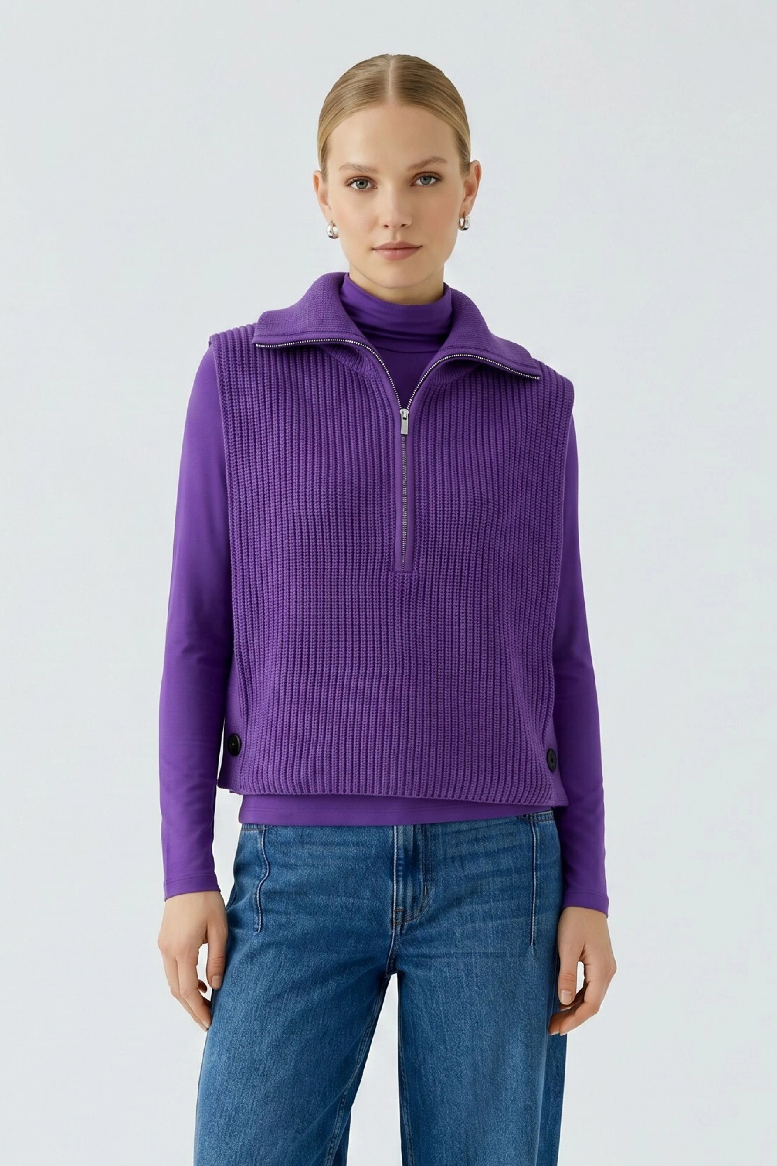 Woman in purple pullunder over turtleneck, paired with blue jeans, standing confidently.