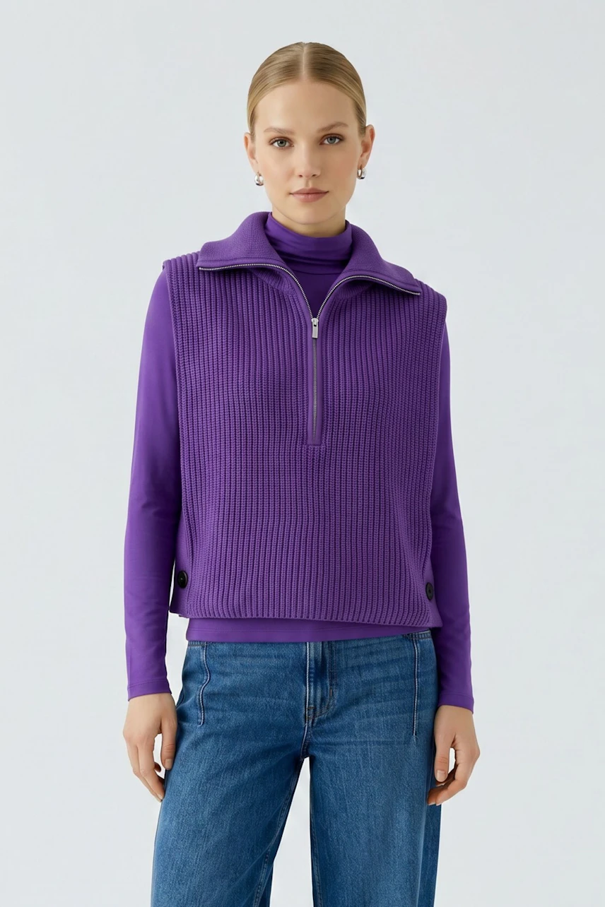 Woman in purple pullunder over turtleneck, paired with blue jeans, standing confidently.