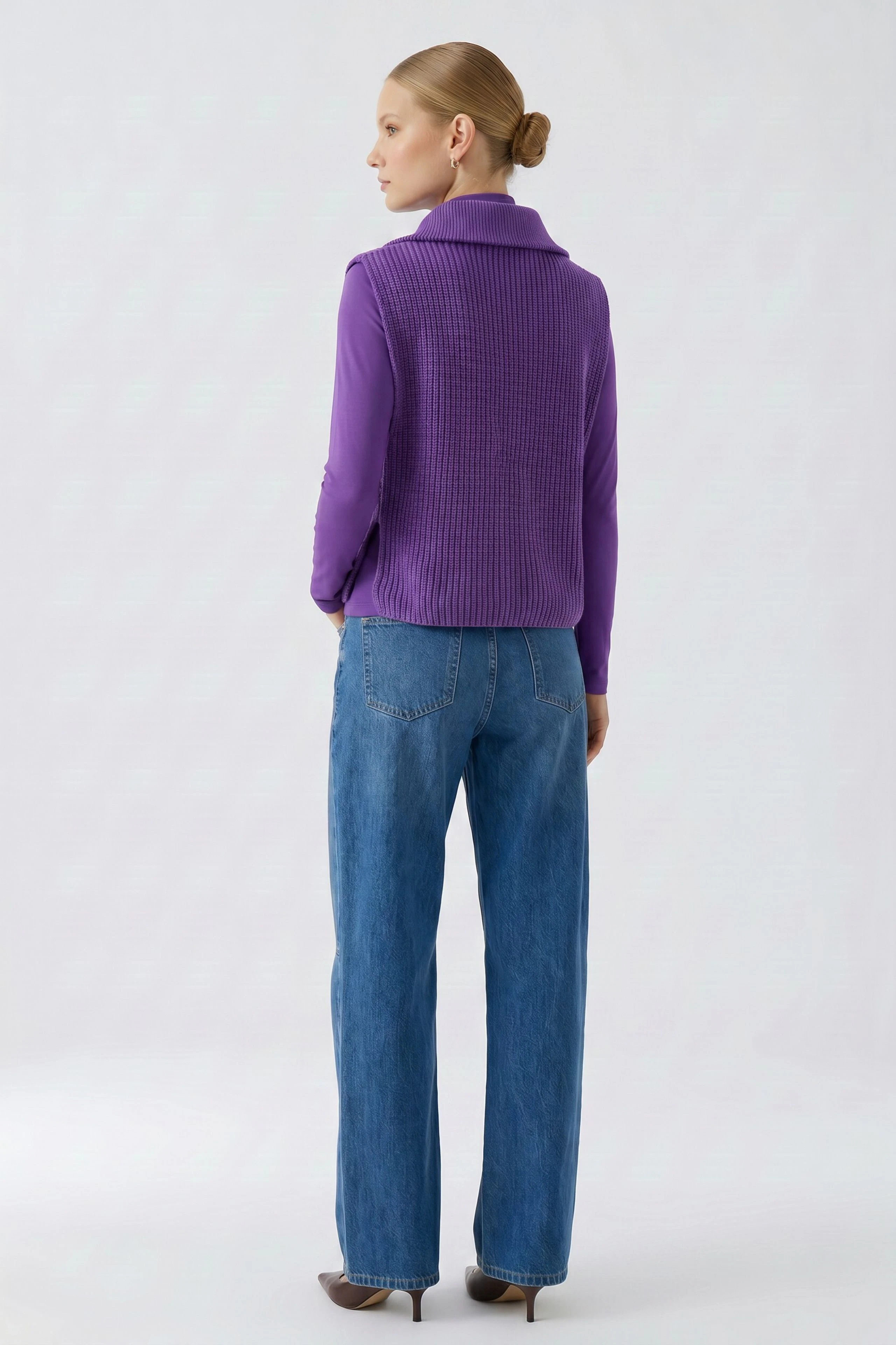 Woman in purple pullunder and blue jeans, viewed from the back, showcasing casual style.