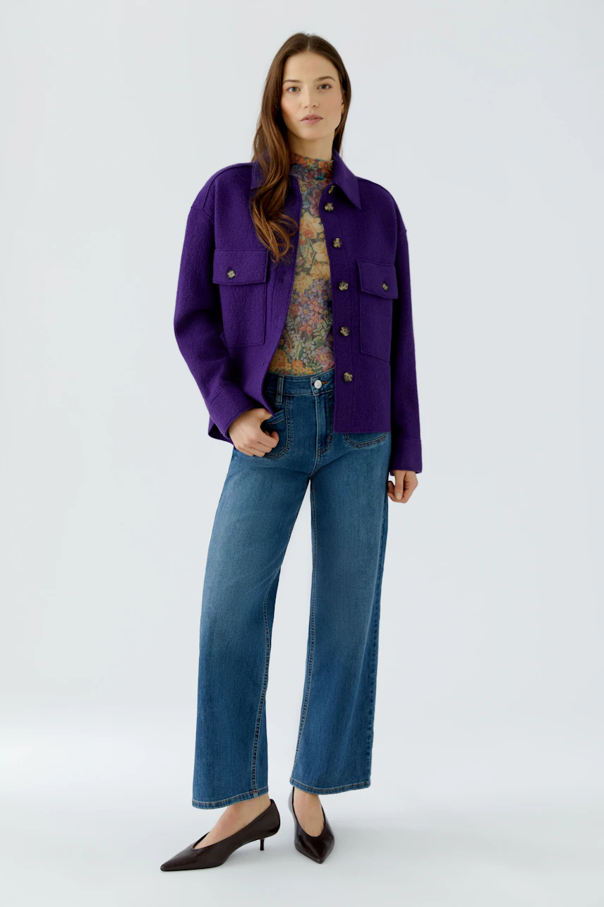 Casual overshirt: Woman in purple overshirt, floral top, and jeans, standing confidently.