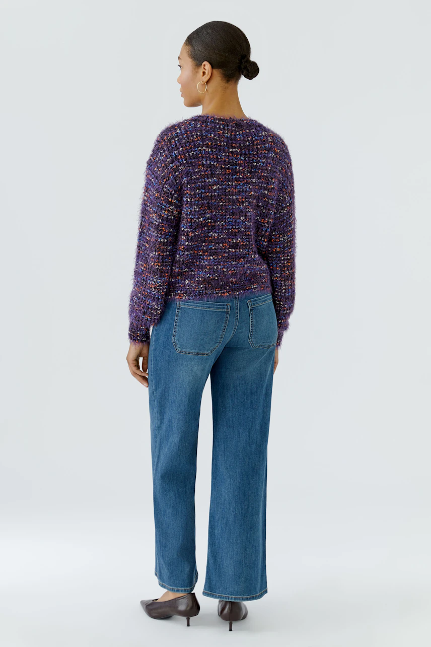 Frau im bunten Pullover und blauer Jeans, von hinten gesehen. Lässiger Look für den Alltag.