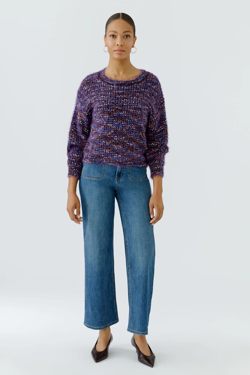 Frau im lässigen, bunten Pullover und Jeans. Der Pullover ist grob gestrickt und farbenfroh.