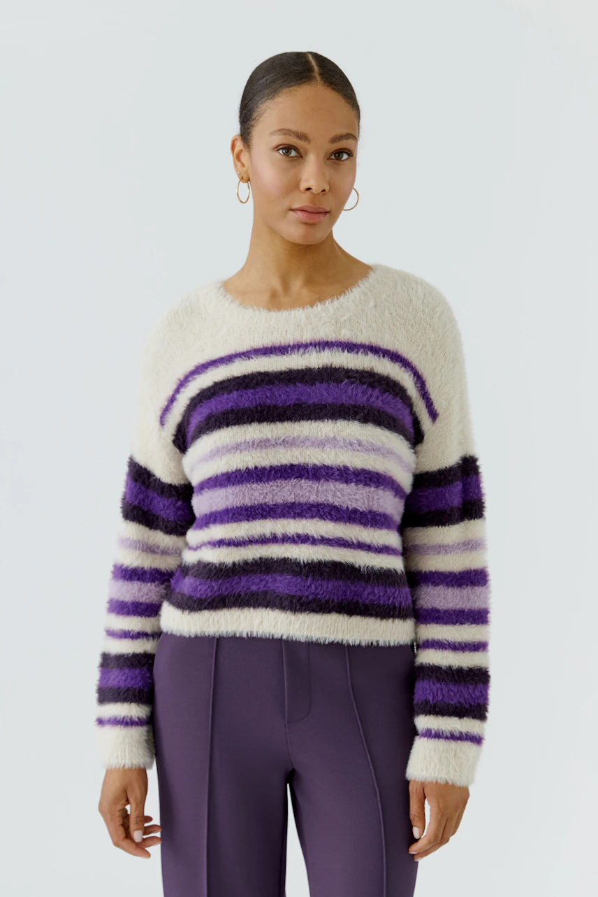 Casual women's pullover: Woman in a fluffy striped pullover with purple and white hues, standing confidently.