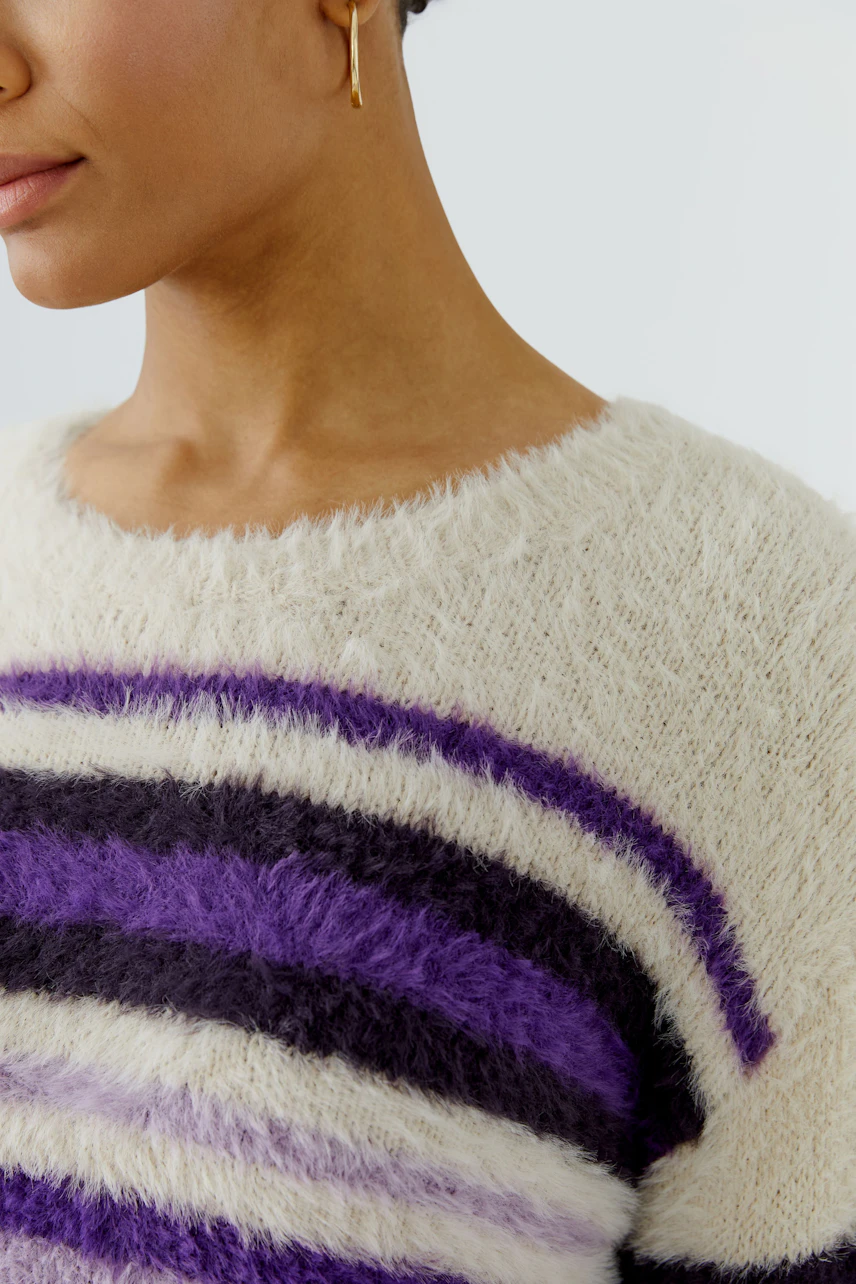 Woman in a cozy striped pullover with purple and black fuzzy stripes, showcasing a casual style.