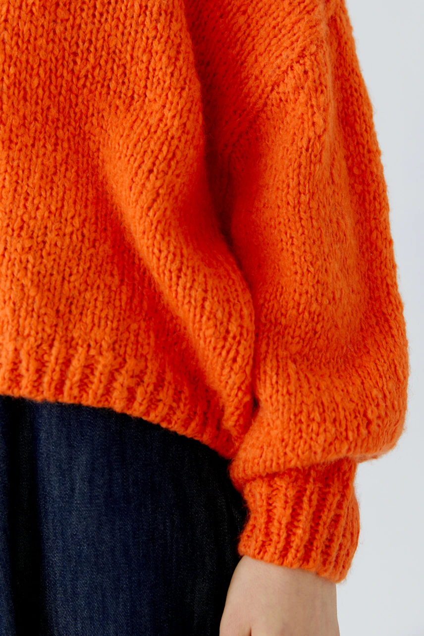 Leuchtend orangefarbener Damen-Pullover aus grobem Strick, kombiniert mit dunkler Jeans.