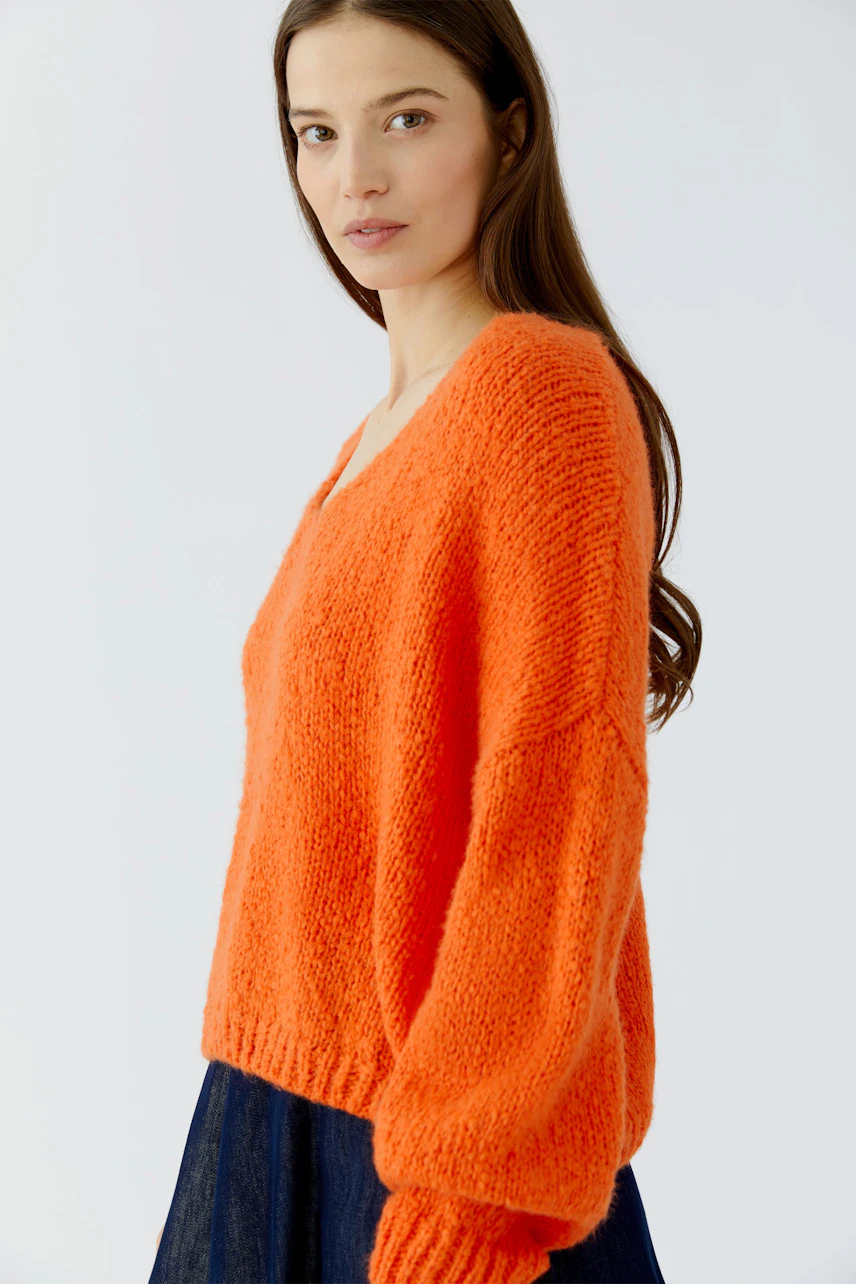 Frau im leuchtend orangefarbenen Pullover, lässig geschnitten, kombiniert mit dunklem Rock.
