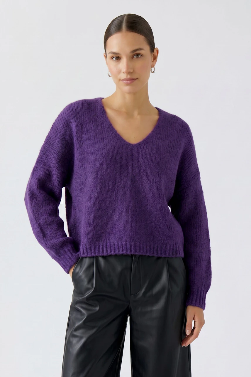 Casual women's pullover: Woman in a purple V-neck pullover with black leather pants, looking confident.