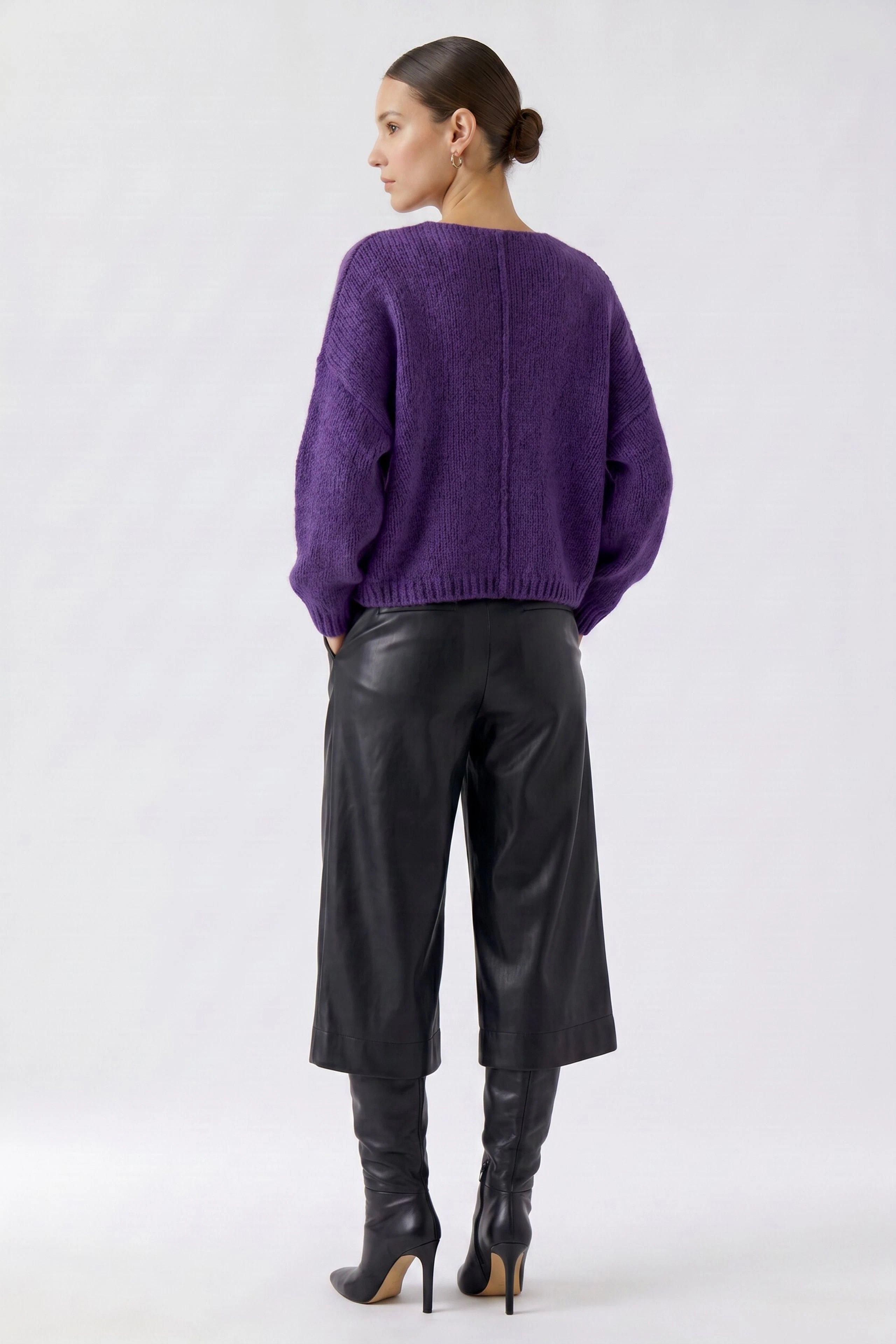 Woman in a purple pullover and black leather pants, viewed from the back, showcasing casual style.