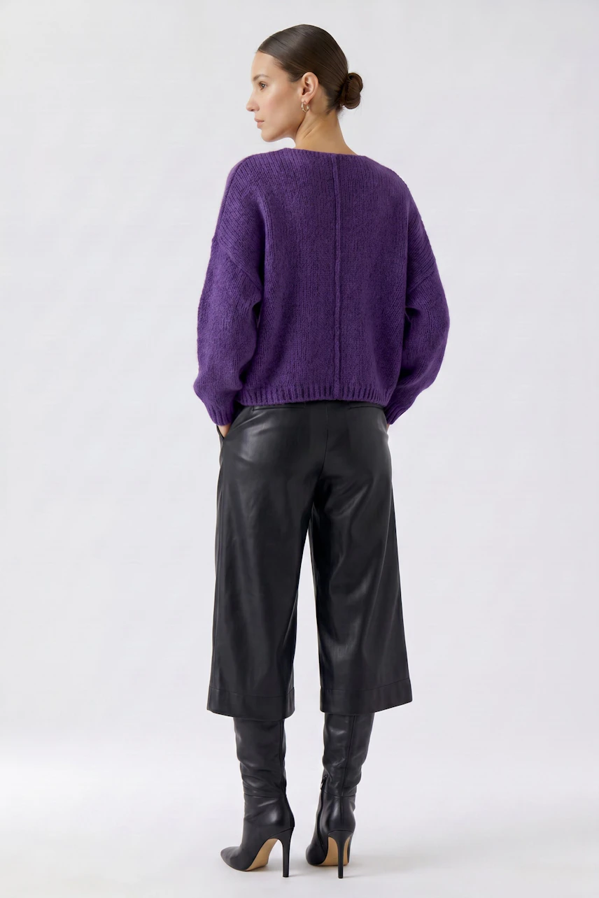 Woman in a purple pullover and black leather pants, viewed from the back, showcasing casual style.