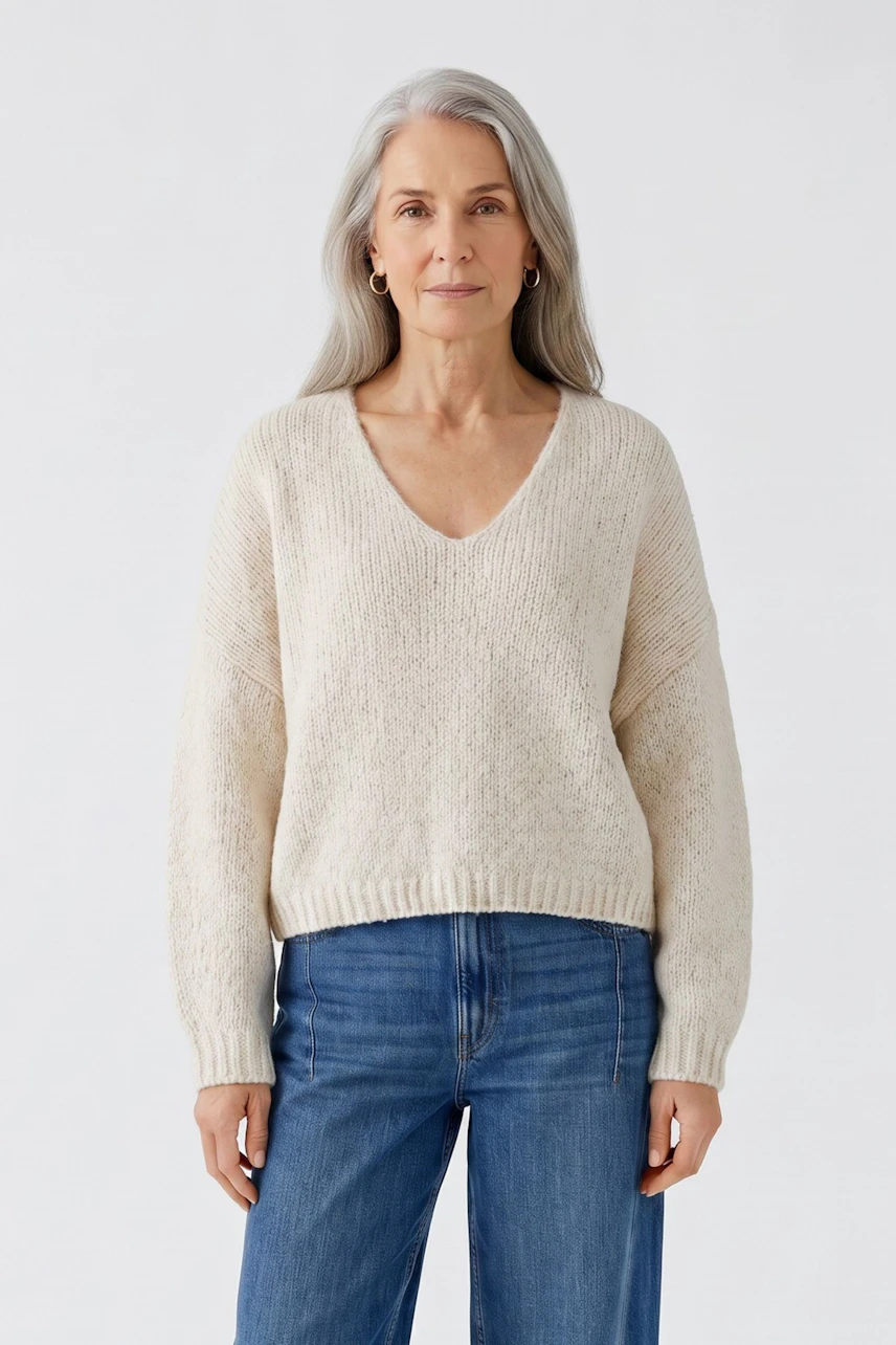 Casual women's pullover: Woman in a cream V-neck pullover and blue jeans, standing confidently.