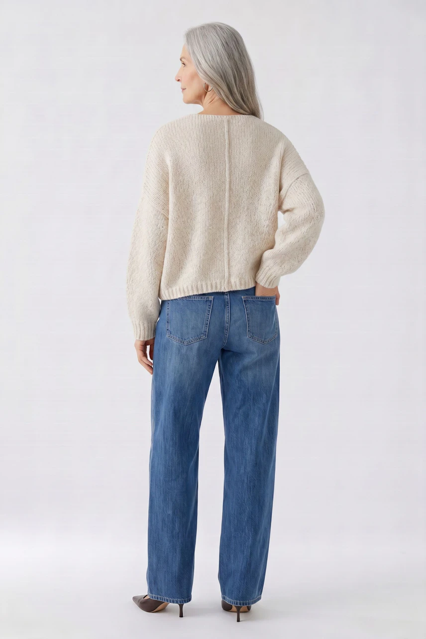 Casual women's pullover: Woman in a beige pullover and blue jeans, standing confidently.