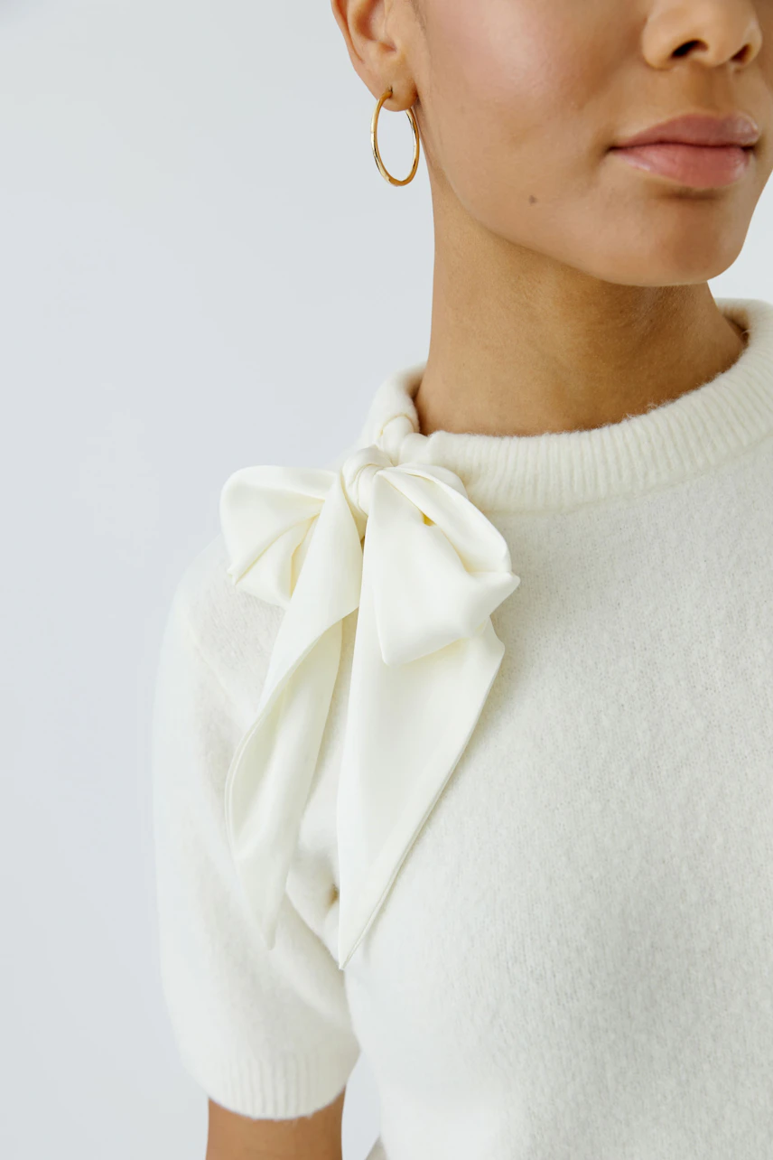 Damen-Pullover: Frau im weißen Pullover mit großer Schleife am Kragen, dezenter Look.