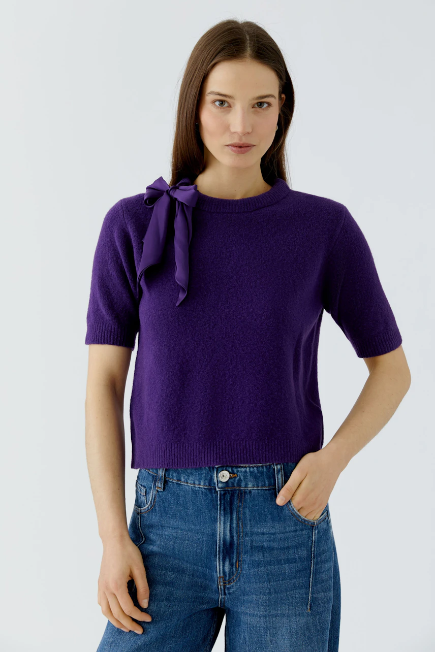 Casual women's pullover: Woman in a purple short-sleeve pullover with a bow detail, paired with jeans.