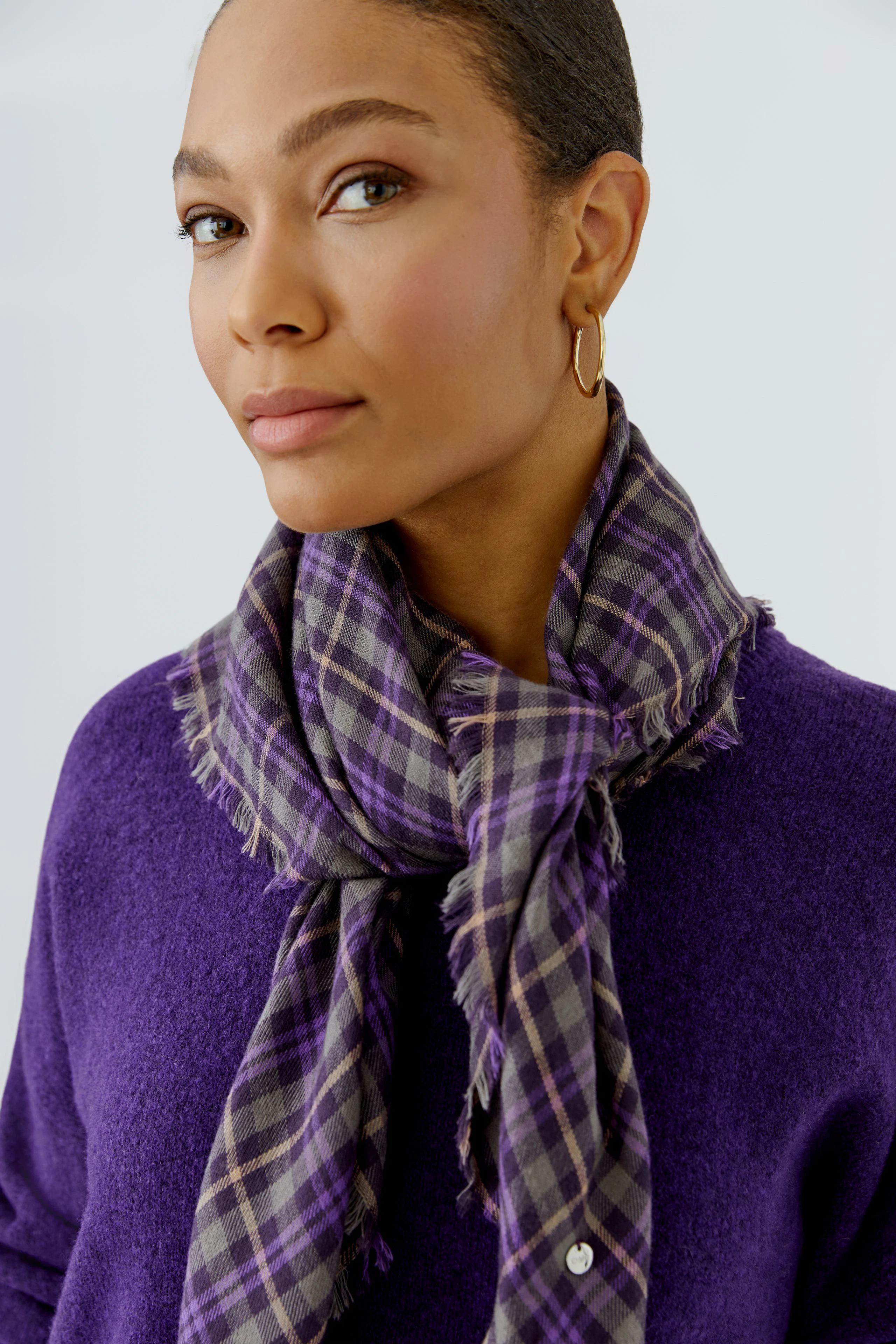 Plaid scarf: Woman in purple pullover with a checkered scarf, looking confidently.