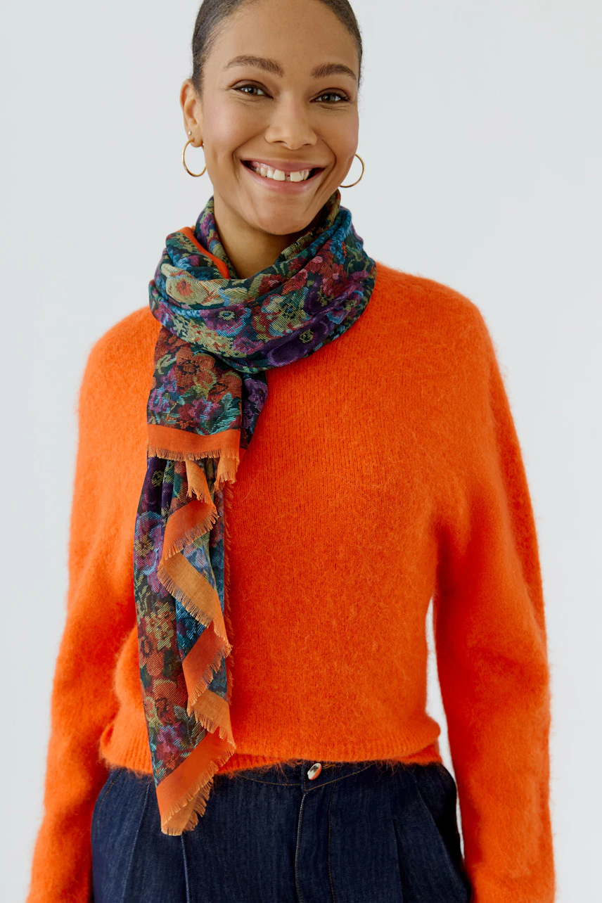 Colorful scarf: Woman in vibrant orange pullover with a floral scarf, smiling confidently.
