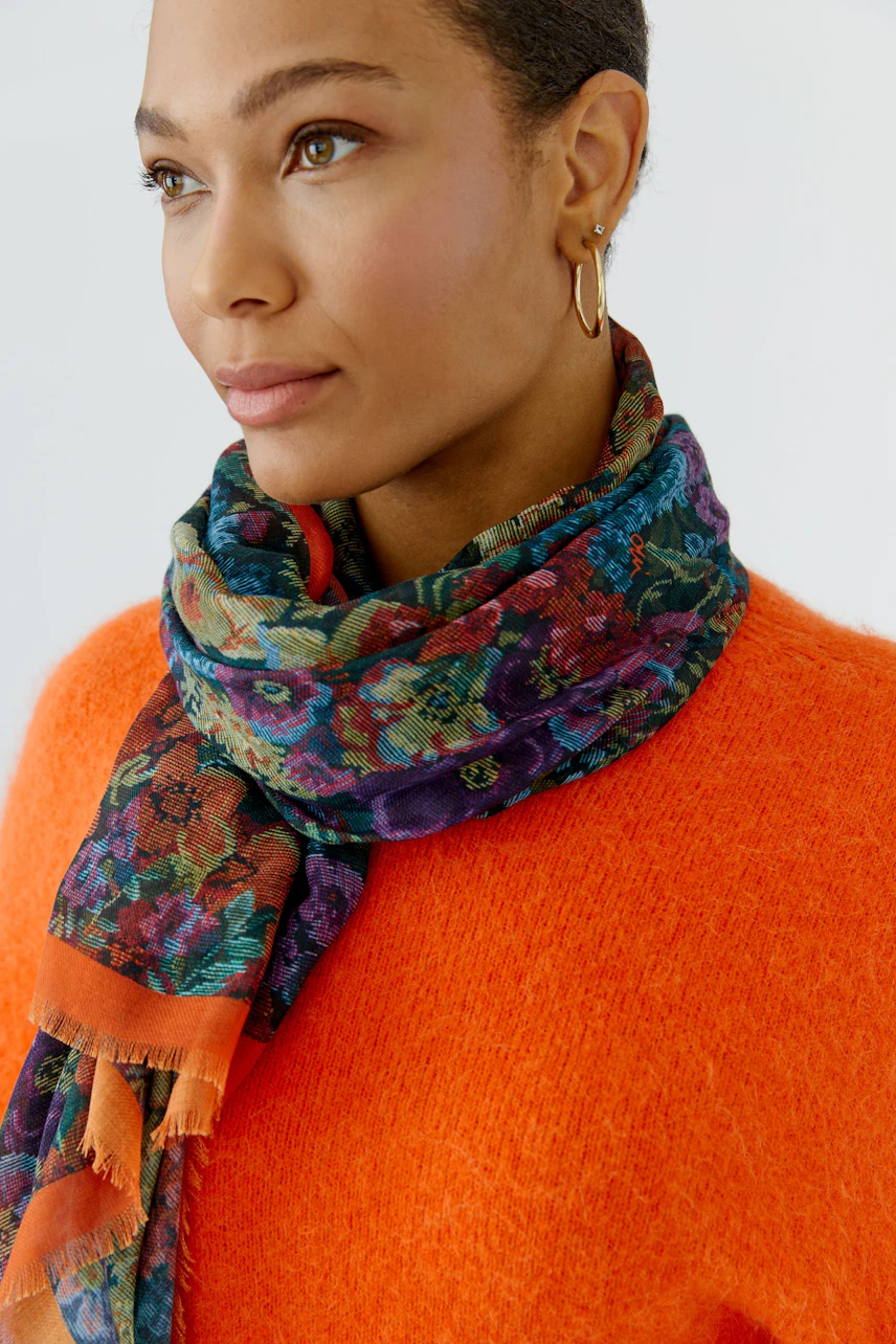 Colorful scarf: Woman in vibrant floral scarf and orange sweater, looking to the side.