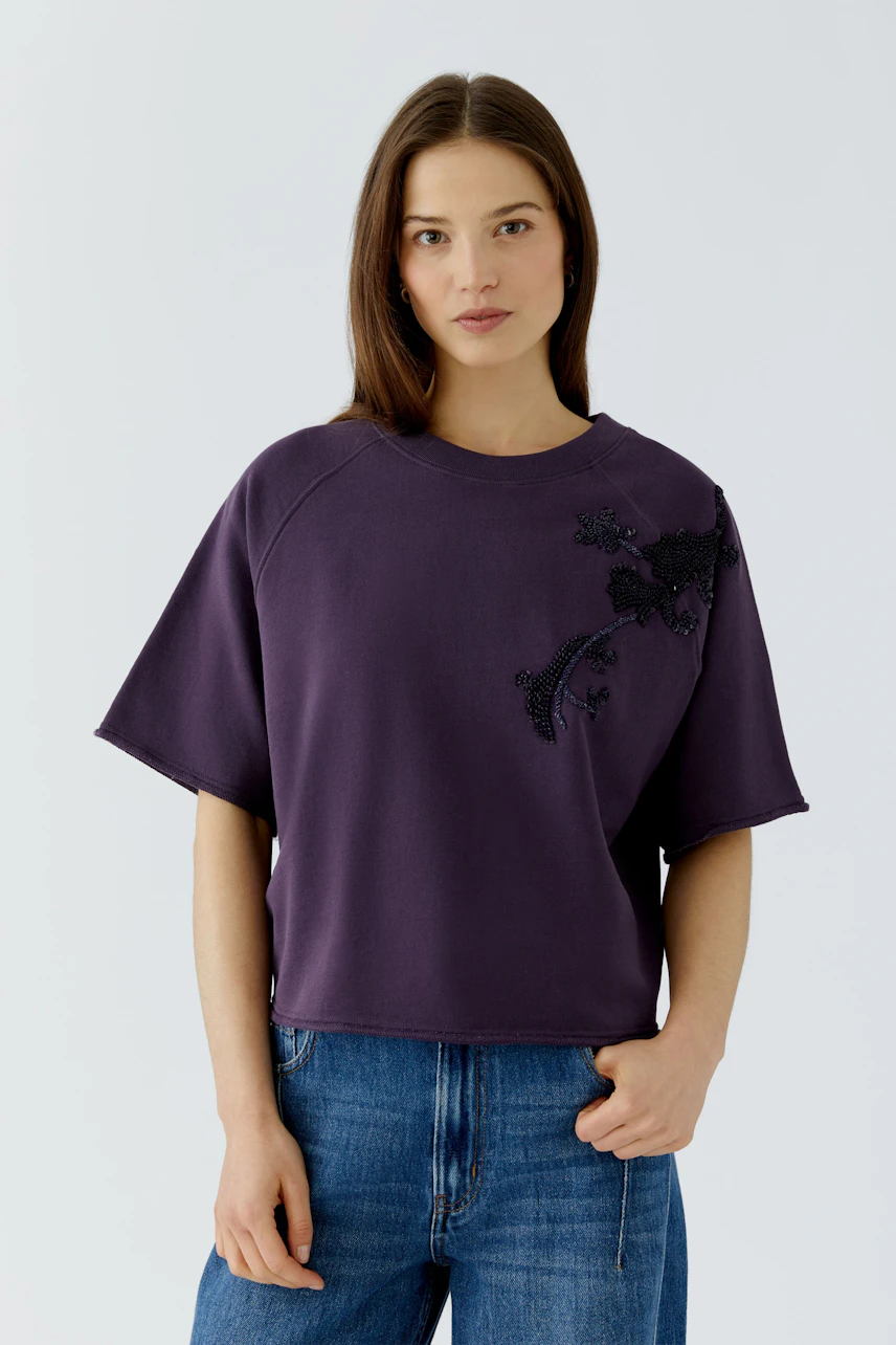 Lässiges Damen-Sweatshirt: Frau im lila Sweatshirt mit floralem Muster und blauer Jeans.