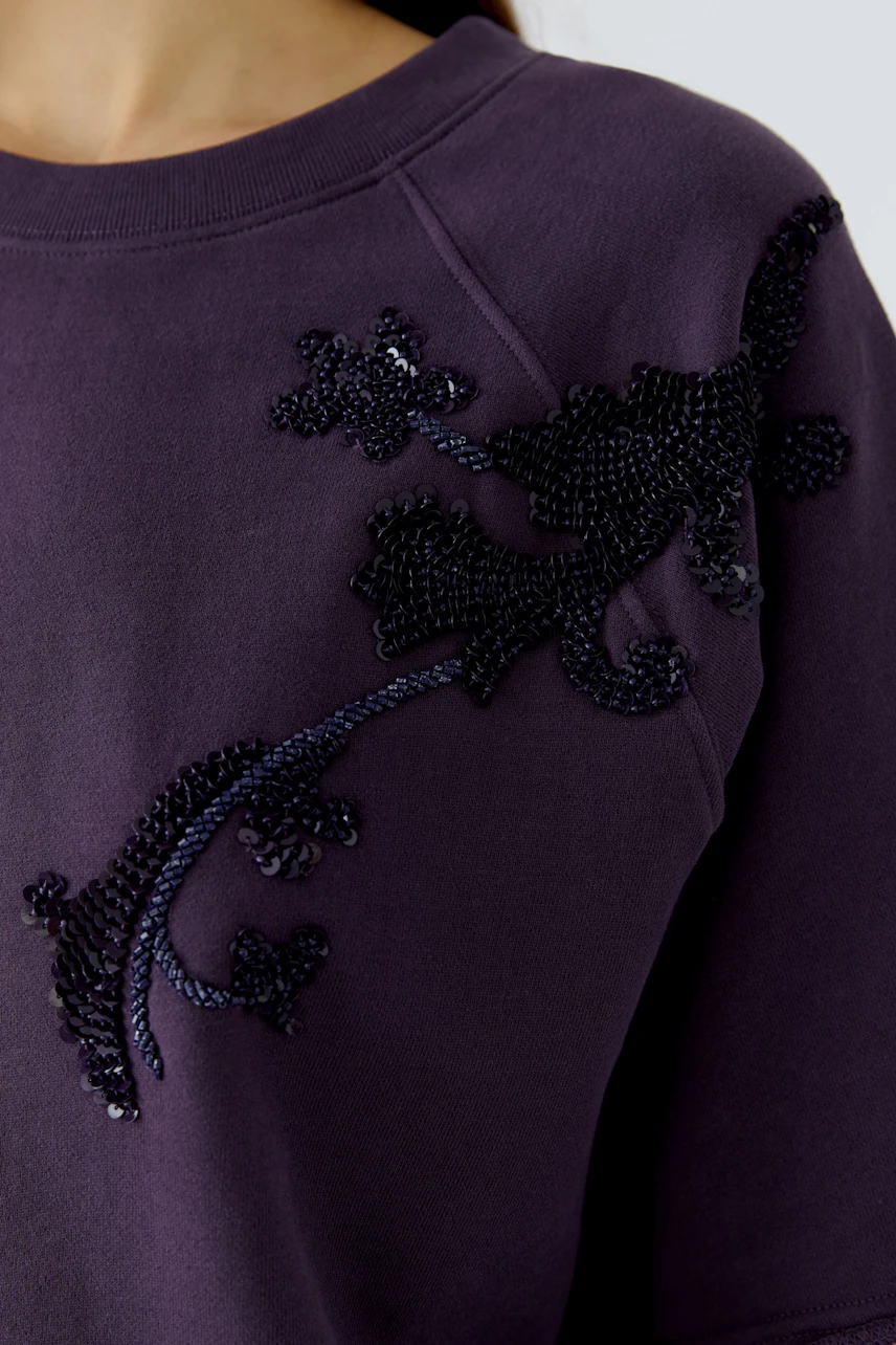 Lila Sweatshirt mit schwarzer Verzierung. Detailaufnahme des Stoffes, keine Frau im Bild.