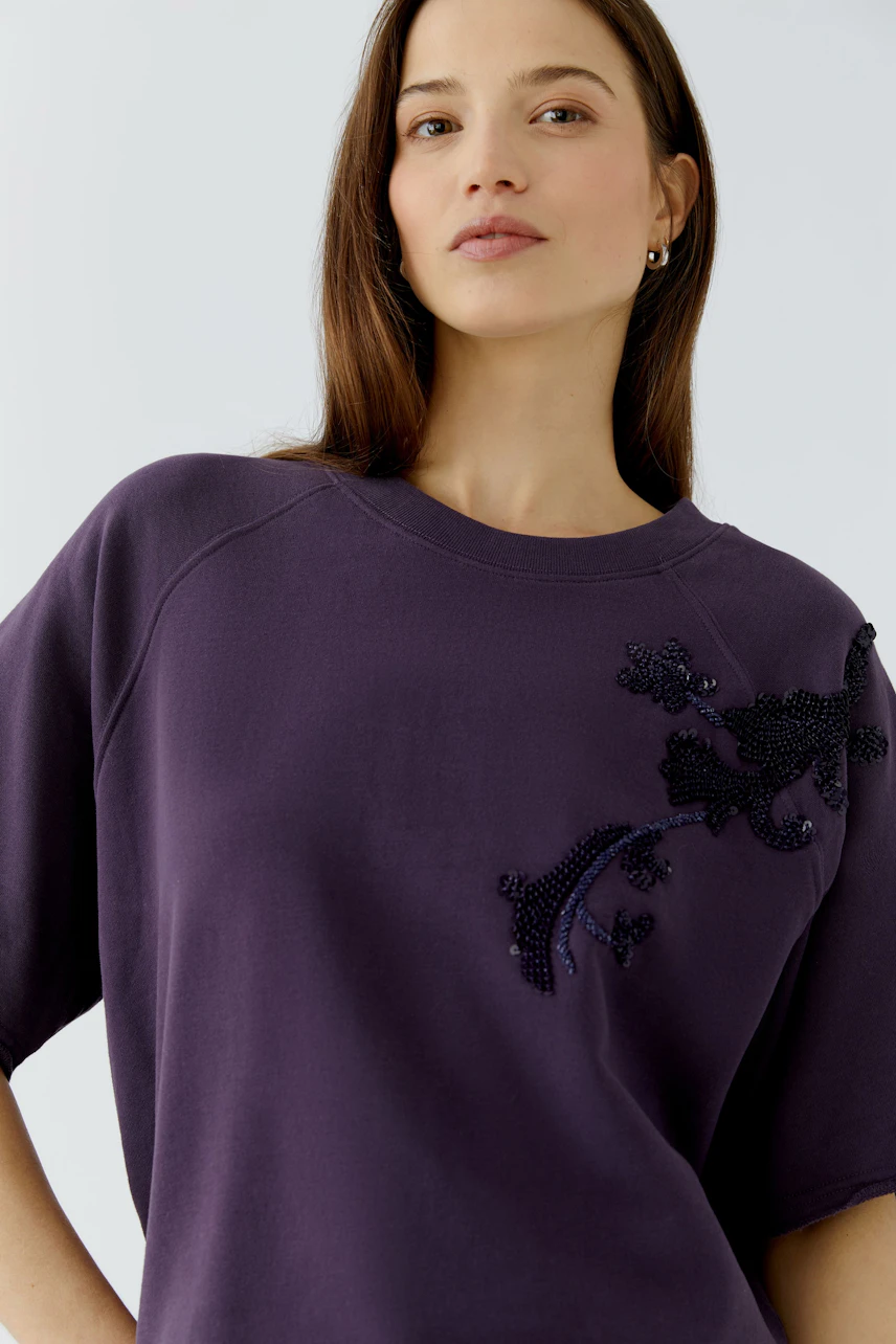 Frau im lila Sweatshirt mit floralen Applikationen, lässig und modern.