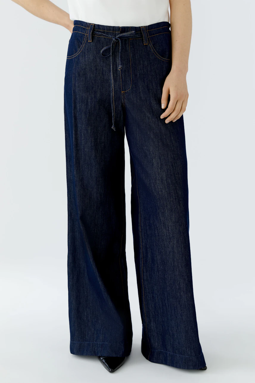 Jeans Wide Leg: Frau in dunkelblauer, weit geschnittener Jeans mit Bindegürtel, lässig und modern.
