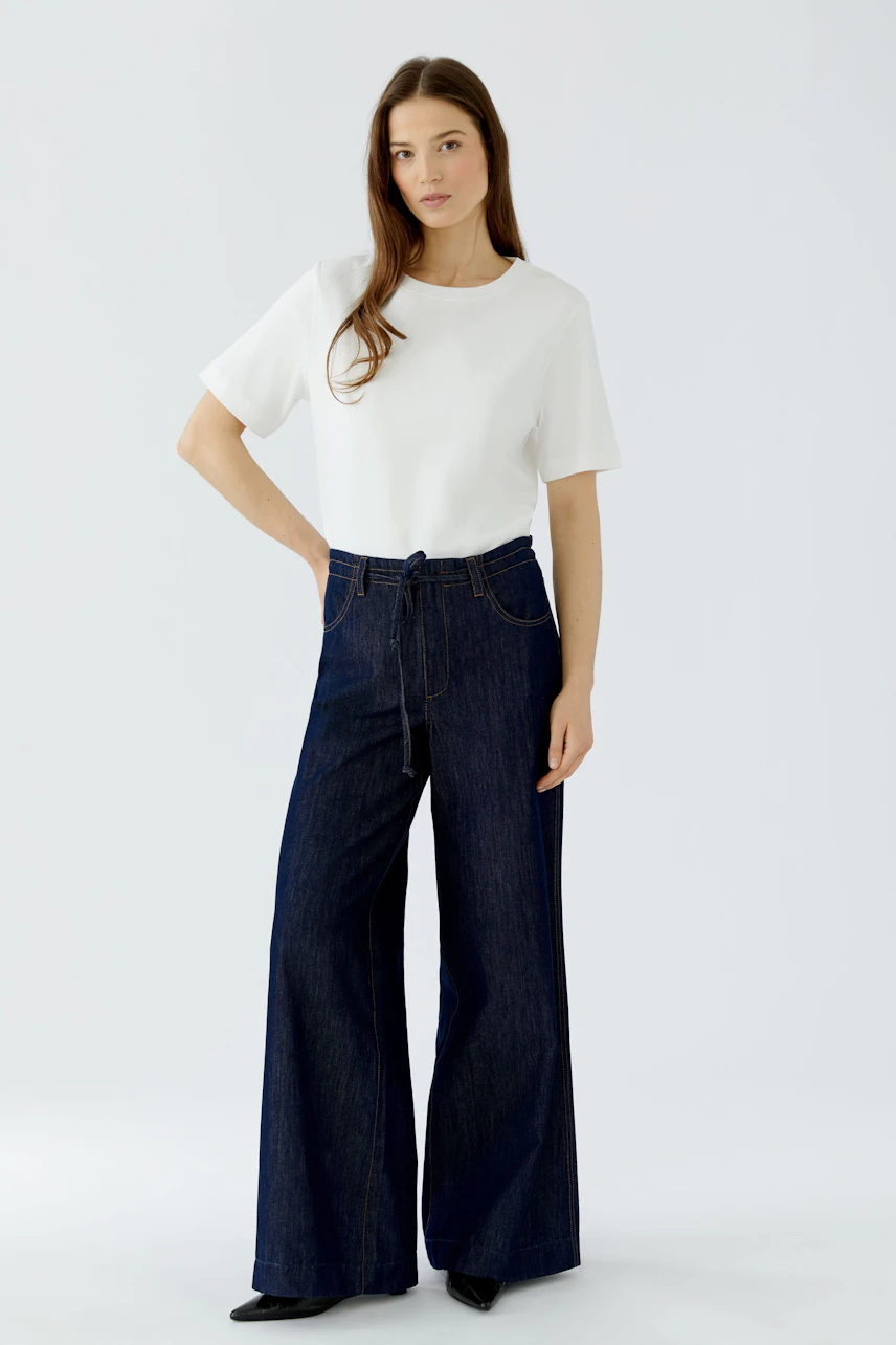 Frau in Jeans Wide Leg: Dunkle, weite Jeans mit weißem T-Shirt, lässiger Look.