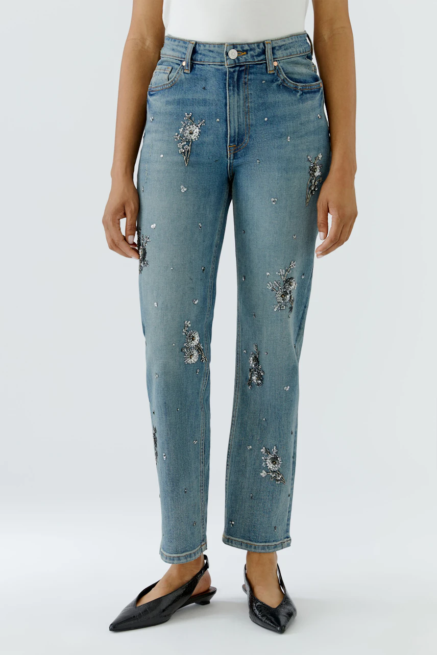 Woman in relaxed jeans with floral embroidery, standing confidently in black flats and white top.
