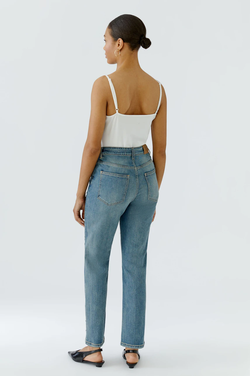 Woman in relaxed jeans and white top, standing confidently. Casual style with a focus on comfort.