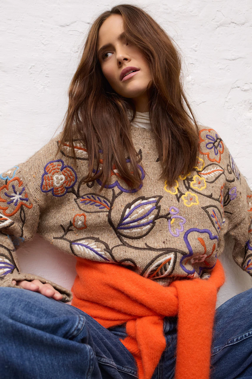 Frau in Jeans Barrel: Lässige Jeans kombiniert mit besticktem Pullover und orangefarbenem Schal.