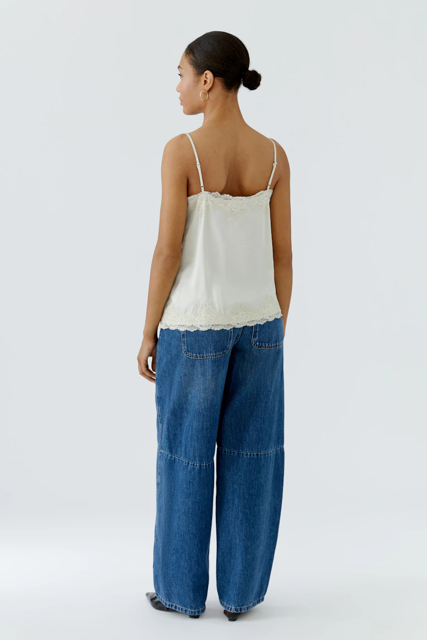 Damen-Top: Frau im weißen Spitzentop mit Spaghettiträgern und blauer Jeans von hinten gesehen.