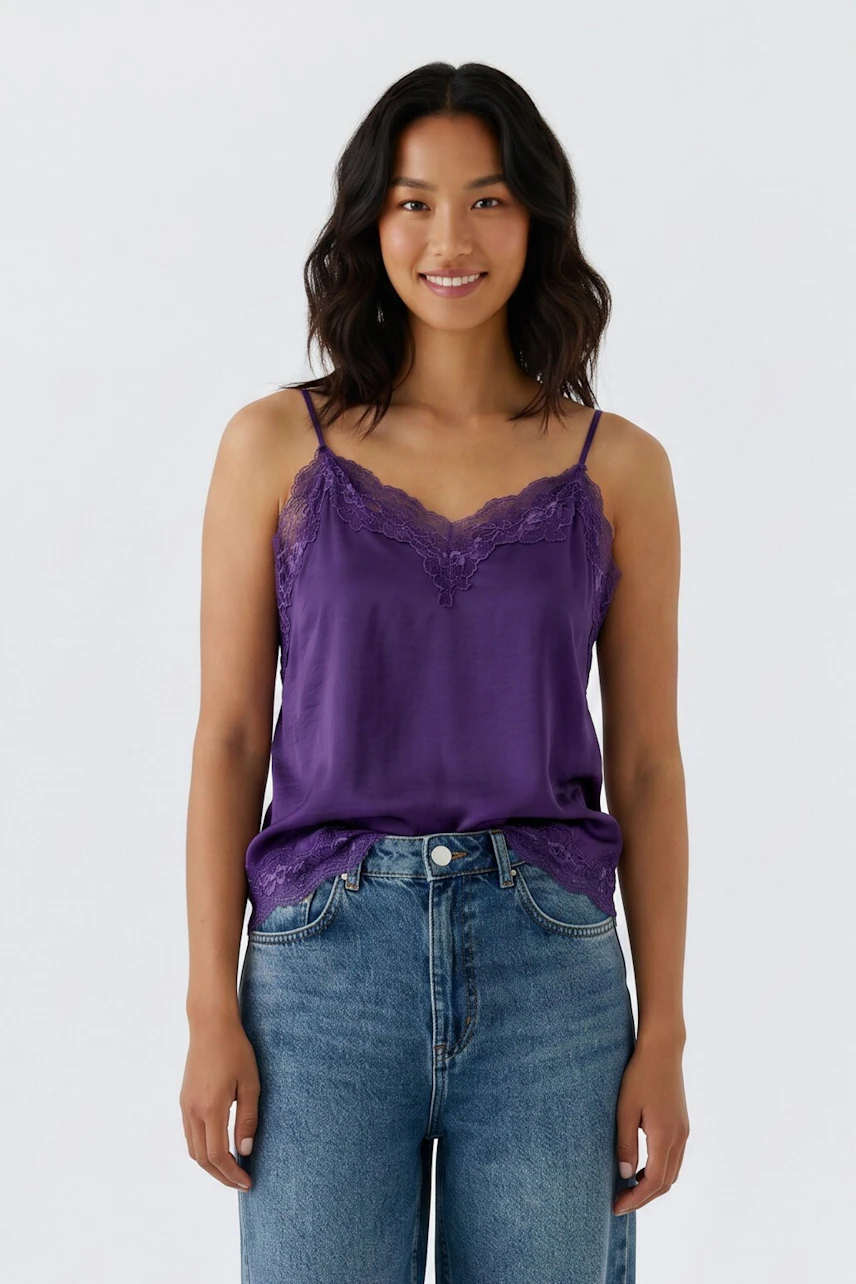 Lässiges Damen-Top: Frau im lila Spitzentop und Jeans, lächelt entspannt.