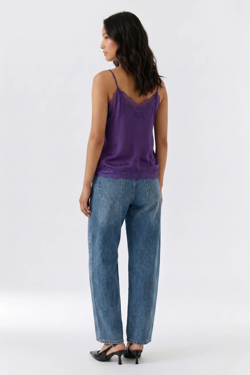 Lässiges Damen-Top: Frau im lila Top mit Spitze und blauer Jeans, seitlich stehend.