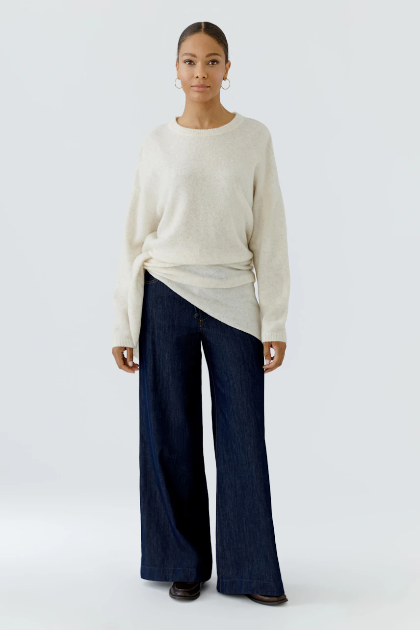 Casual scarf: Woman in a cozy beige pullover and wide-leg jeans, showcasing a stylish accessory.