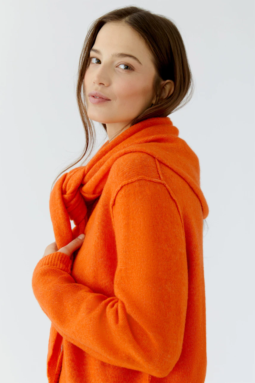 Bright orange scarf: Woman wearing a cozy orange scarf over a matching pullover, looking relaxed.