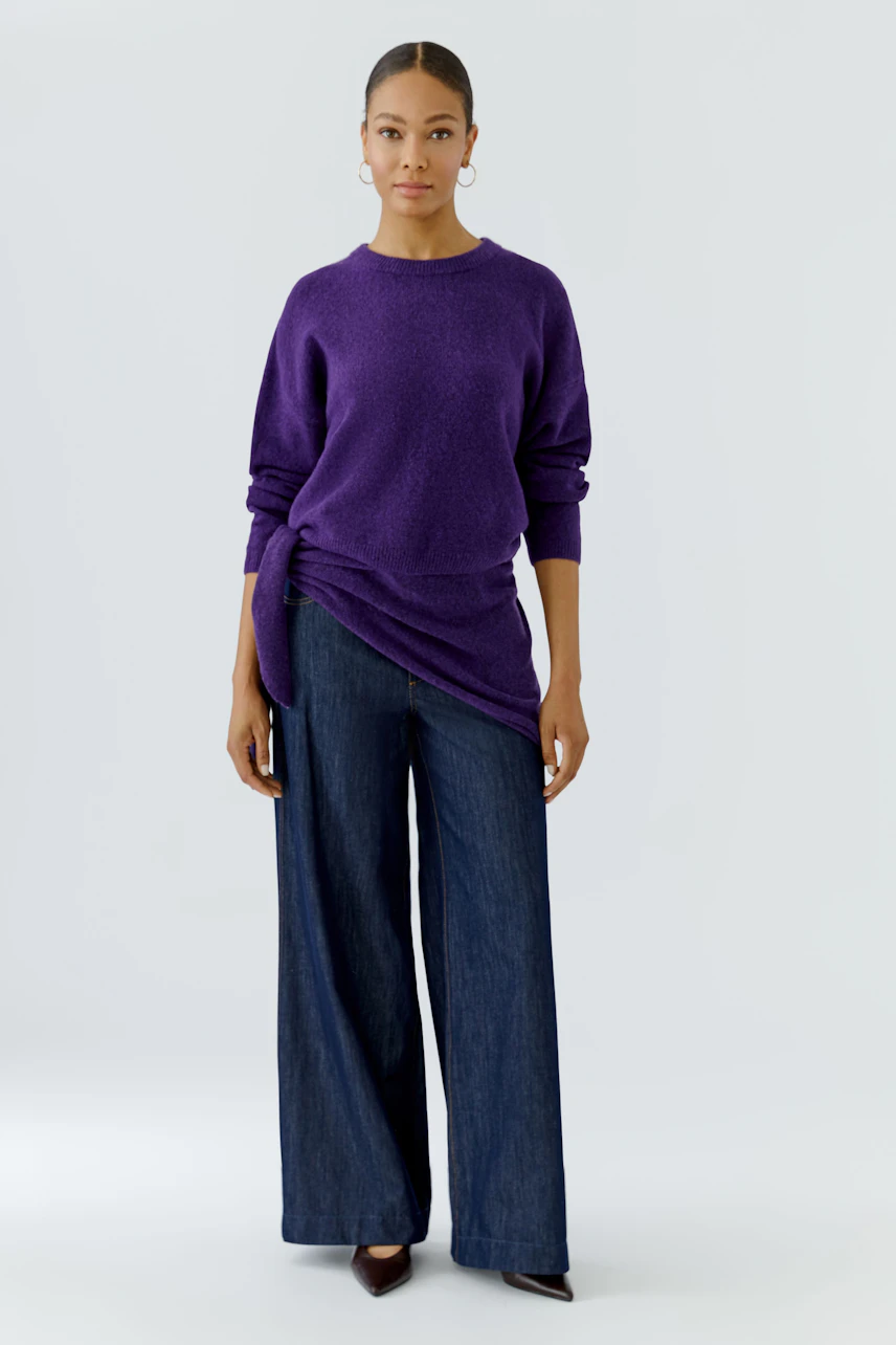 Casual scarf: Woman in a purple pullover and wide-leg jeans, showcasing a relaxed style.