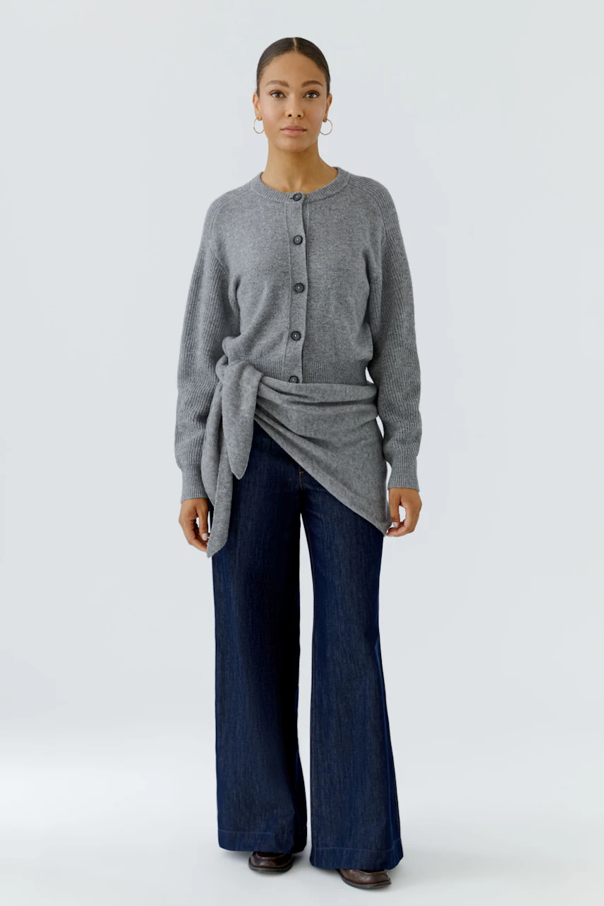 Woman in a cozy gray cardigan and wide-leg jeans. The cardigan features a stylish tie detail.