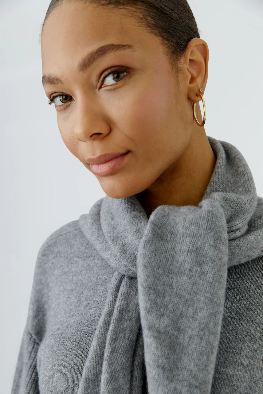 Woman in a cozy gray scarf, paired with a matching pullover, looking confidently at the camera.