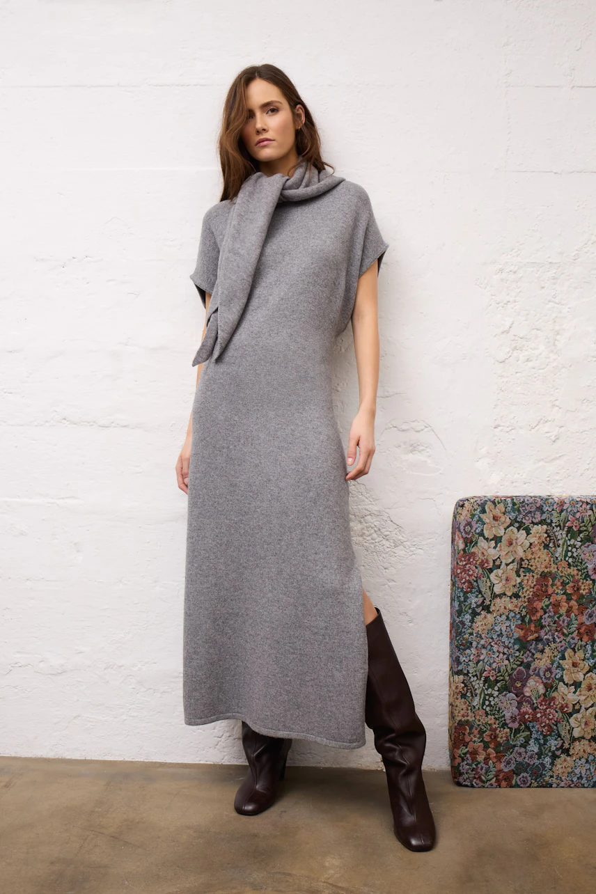 Woman in a grey dress with matching scarf, standing confidently in brown boots.