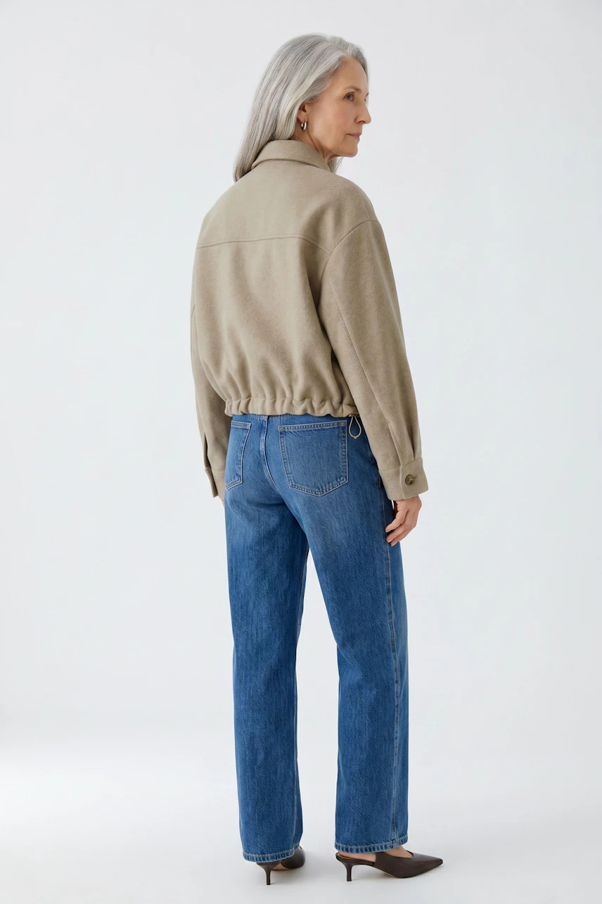 Casual women's jacket: Woman in beige jacket and blue jeans, standing confidently.