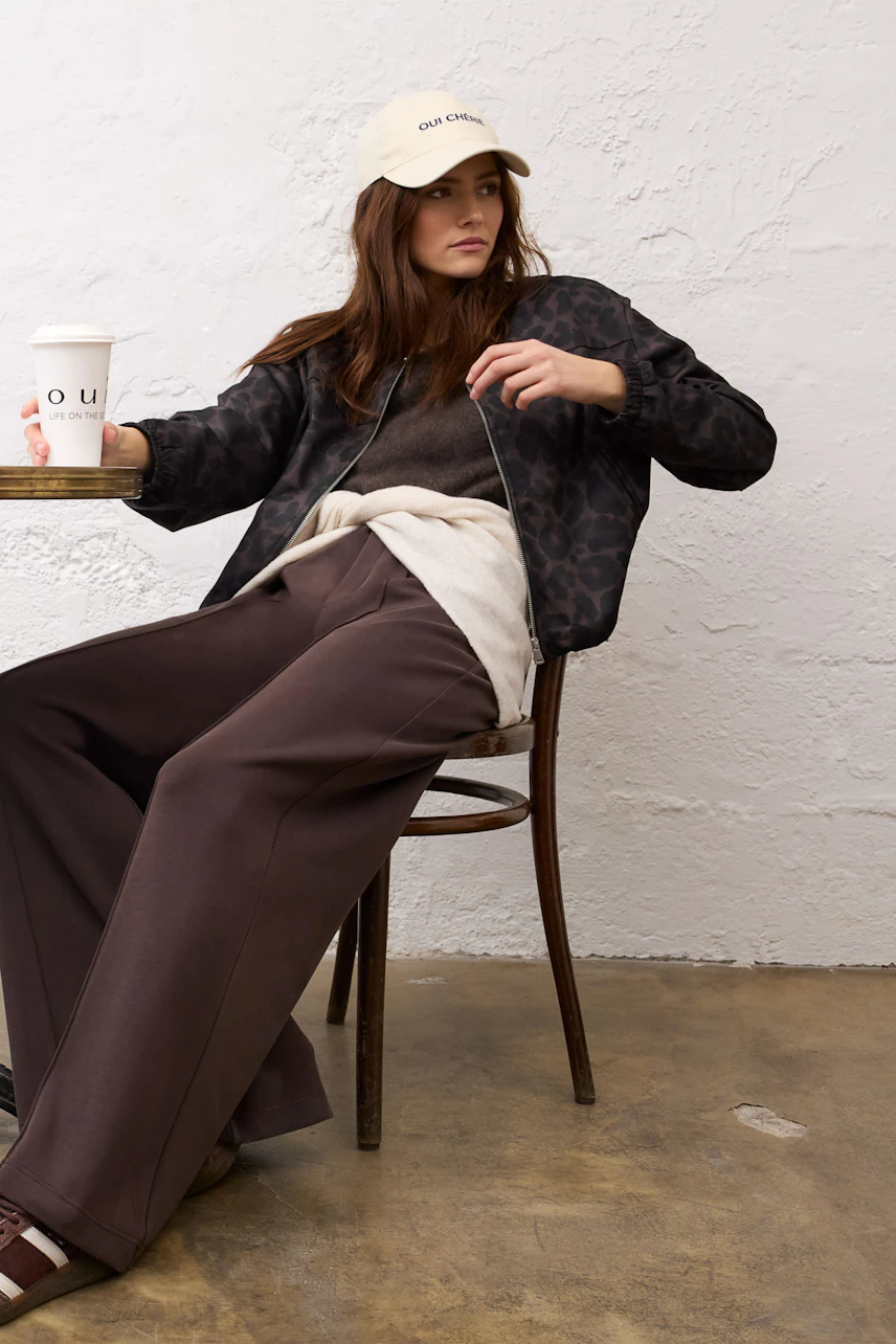 Casual blouson: Woman in a dark patterned blouson, relaxed fit, paired with wide brown pants and a cap.